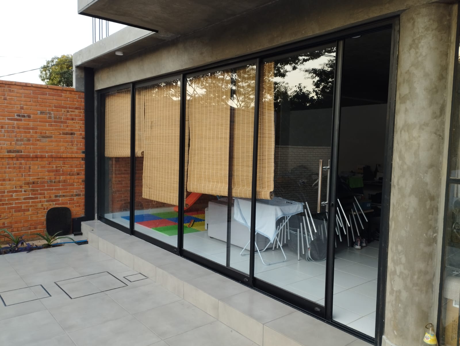 Cerramiento de vidrio corredizo con aluminio negro en patio con muro de ladrillo — MÁS VIDRIOS